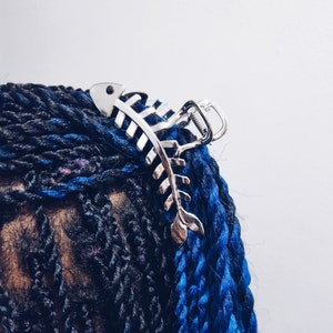 May include: A silver fishbone-shaped hair clip holding back blue and black braided hair.