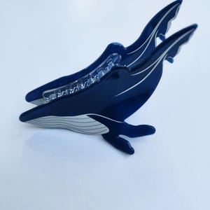 May include: A blue whale hair clip with a white underbelly and a clear plastic clip on the back.