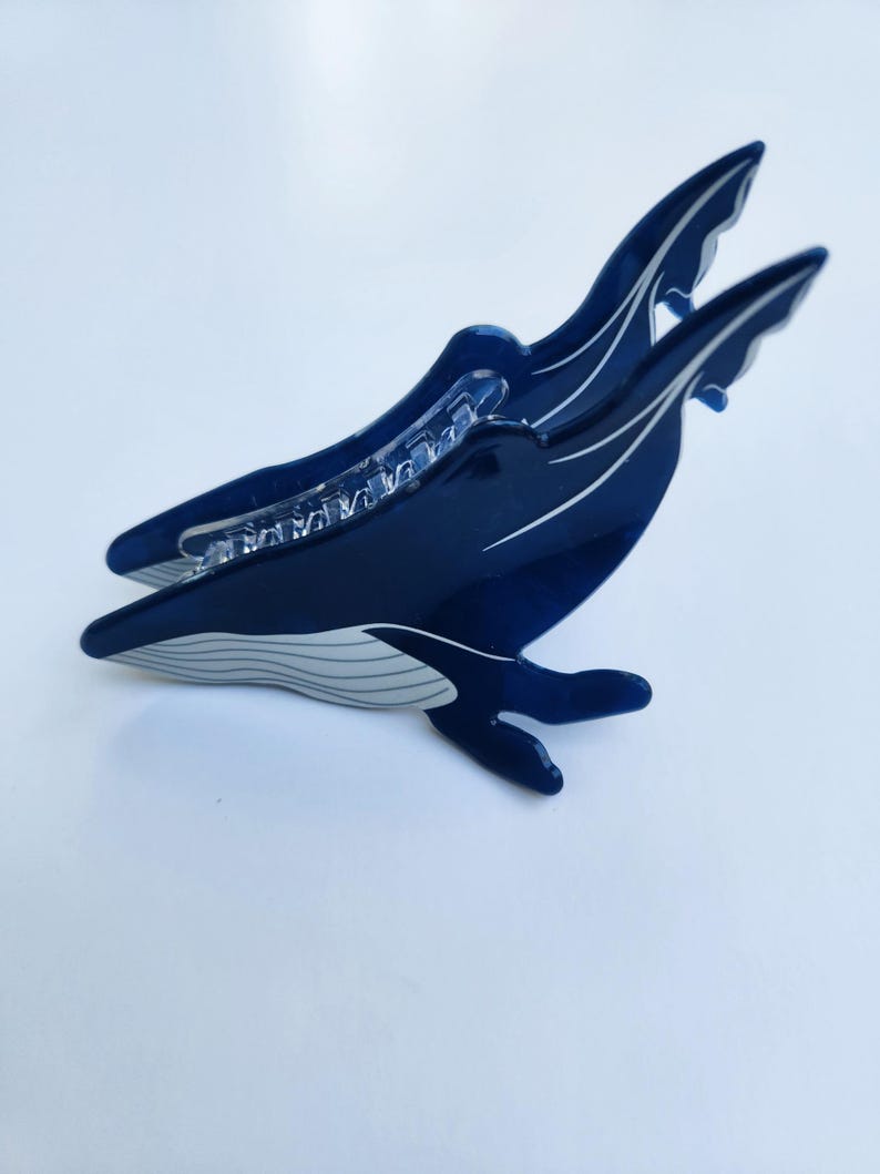 May include: A blue whale hair clip with a white underbelly and a clear plastic clip on the back.