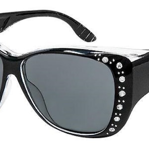 May include: Black sunglasses with rhinestones on the side and a clear frame. The sunglasses have a black, textured design on the arms.