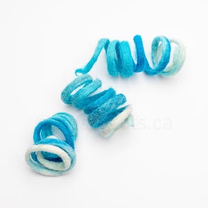 May include: Three blue and white felt yarn coils, each with a different shape and size. The coils are arranged on a white background.