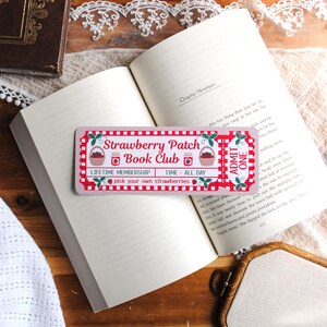 Peut inclure: Un marque-page rectangulaire conçu comme un billet vintage avec une bordure à carreaux rouges et blancs. Il présente le texte Strawberry Patch Book Club, ADMIT ONE, LIFETIME MEMBERSHIP, TIME: ALL DAY et pick your own strawberries avec des illustrations.