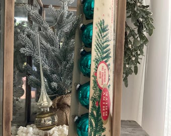 May include: A set of six teal blue Shiny Brite glass Christmas tree ornaments in a vintage box. The box has a green pine tree illustration and the text "Shiny Brite Class Christmas Tree Ornaments American Made".