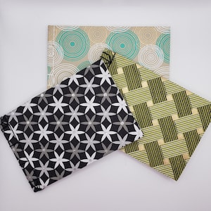 May include: Three decorative notebooks with patterned covers. One has a black and white floral design, another features a green and gold woven pattern, and the third has teal and gold concentric circles on a tan background.