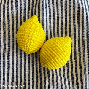 May include: Two crocheted lemon-shaped toys on a striped background. The lemons are yellow and have a textured surface.