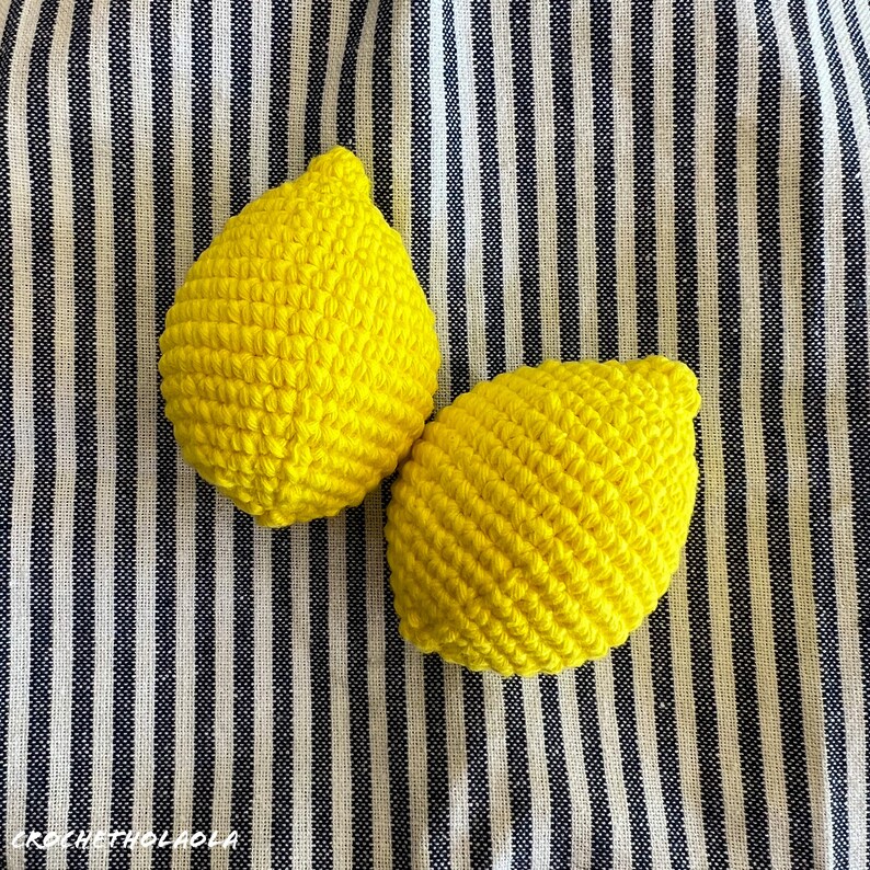 May include: Two crocheted lemon-shaped toys on a striped background. The lemons are yellow and have a textured surface.