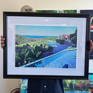 May include: A framed painting of a colorful landscape with a pool and a house in the distance. The painting is set against a blue sky and ocean.