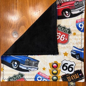 May include: A cream-colored fabric with a vintage road trip theme. It features blue and red cars, Route 66 signs, and a traffic light. The fabric has a black backing.