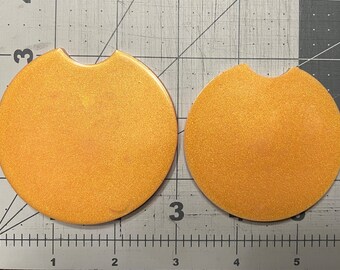 May include: Two gold glitter round coasters with a cut-out for a cup. The coasters are on a gray grid background.