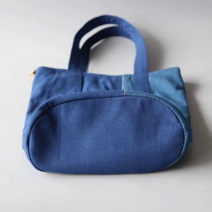 May include: A blue tote bag with two handles. The bag is made of a sturdy fabric and has a rounded bottom. The bag is a solid blue color with a lighter blue accent on the side. The handles are a darker shade of blue.