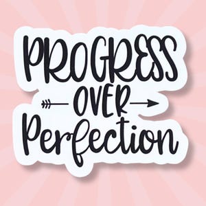 May include: A white sticker with the phrase "PROGRESS OVER PERFECTION" in black script lettering. An arrow graphic separates the words. The sticker is set against a pink background with radiating lines.