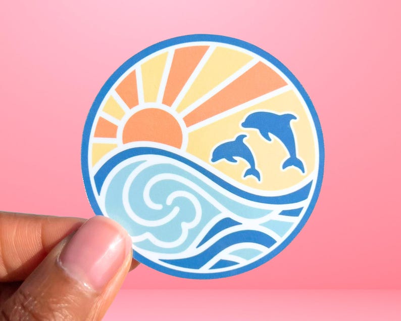 Puede incluir: Una pegatina redonda con una puesta de sol azul, blanca y naranja sobre una ola azul con dos delfines saltando fuera del agua.