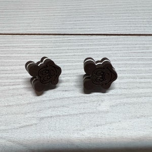 K&ouml;nnte beinhalten: Zwei braune und wei&szlig;e Ohrringe in Keksform mit einem Comic-Gesicht auf jedem. Die Kekse sind &uuml;bereinander gestapelt.