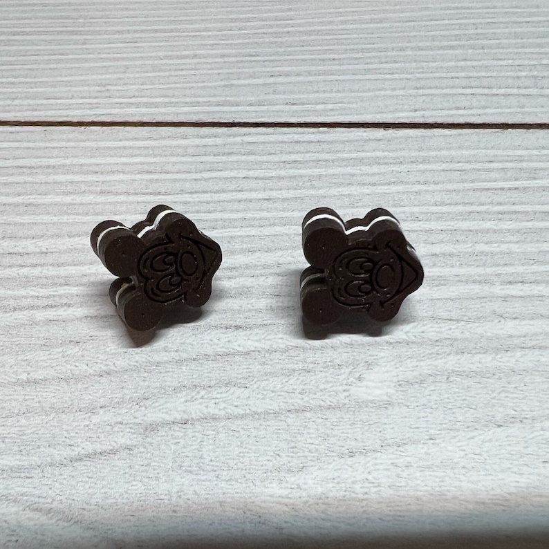 K&ouml;nnte beinhalten: Zwei braune und wei&szlig;e Ohrringe in Keksform mit einem Comic-Gesicht auf jedem. Die Kekse sind &uuml;bereinander gestapelt.