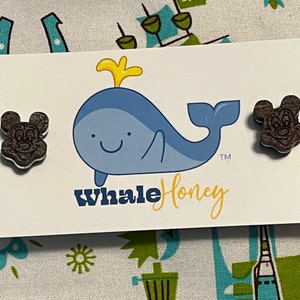 K&ouml;nnte beinhalten: Ein Paar Mickey Mouse Ohren aus Holz mit einem blauen Wal-Logo, auf dem "Whale Honey" und ein Warenzeichen stehen.