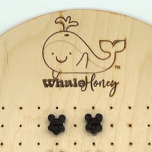 K&ouml;nnte beinhalten: Ein Paar Holzohrringe mit einem schwarz-wei&szlig;en Mickey-Maus-Motiv. Die Ohrringe werden auf einem Holzbrett mit einem Wal-Logo und dem Text "Whale Honey" pr&auml;sentiert.