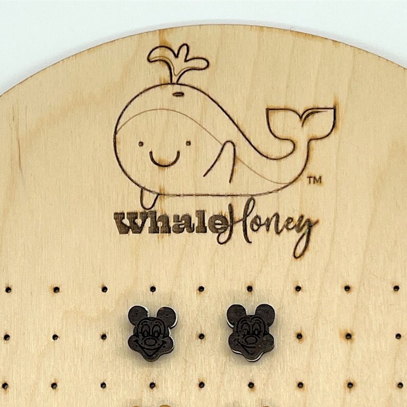 K&ouml;nnte beinhalten: Ein Paar Holzohrringe mit einem schwarz-wei&szlig;en Mickey-Maus-Motiv. Die Ohrringe werden auf einem Holzbrett mit einem Wal-Logo und dem Text "Whale Honey" pr&auml;sentiert.