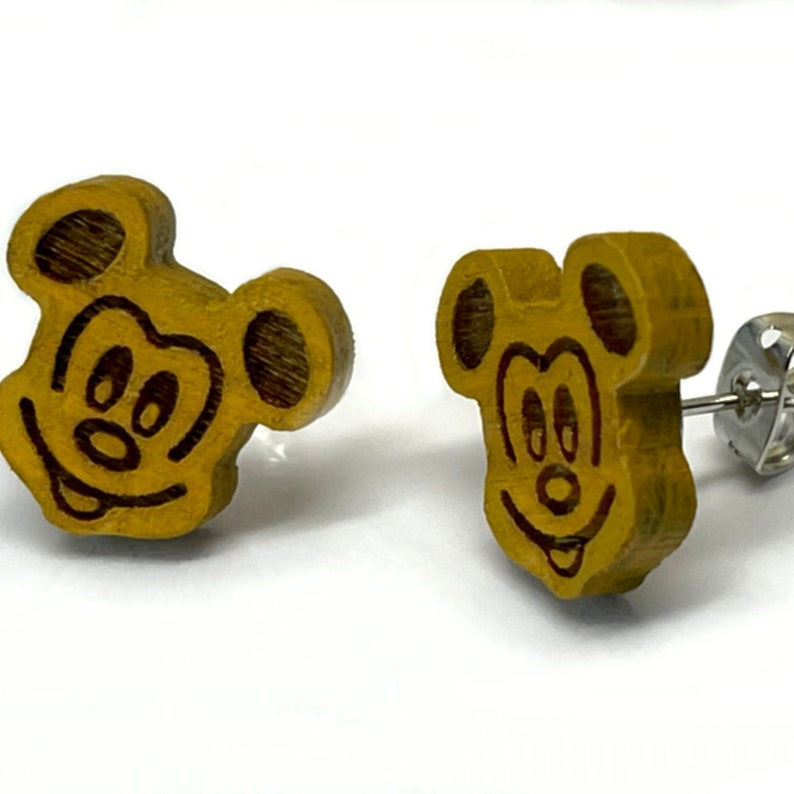 May include: A pair of wooden Mickey Mouse stud earrings. The earrings are yellow with a brown outline and a black face. The earrings are attached to silver posts.