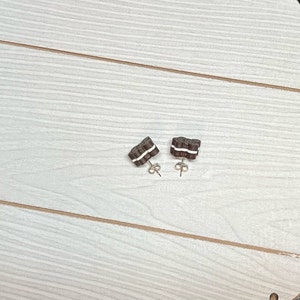 K&ouml;nnte beinhalten: Ein Paar braune und wei&szlig;e Ohrringe in Keksform mit goldenen Stiften.