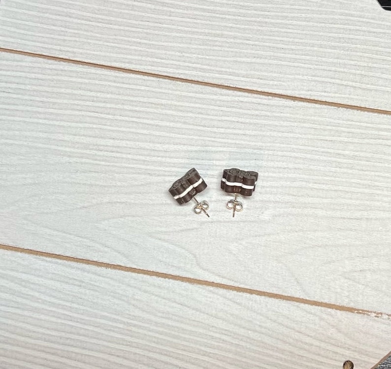 K&ouml;nnte beinhalten: Ein Paar braune und wei&szlig;e Ohrringe in Keksform mit goldenen Stiften.