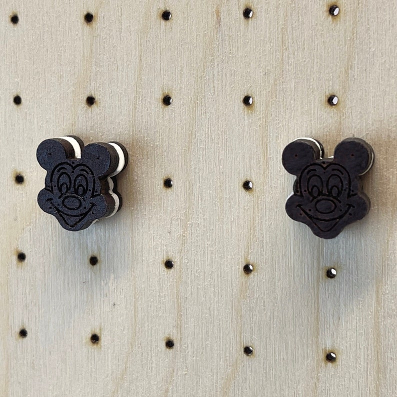 K&ouml;nnte beinhalten: Zwei Ohrringe aus Holz in Form von Mickey Mouse Kopf. Die Ohrringe sind schwarz und wei&szlig; bemalt, um einem Oreo-Keks zu &auml;hneln.