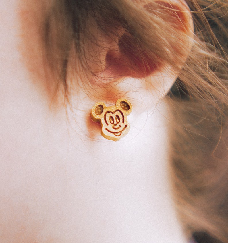 May include: A pair of gold-colored Mickey Mouse earrings. The earrings are made of wood and have a detailed design of Mickey Mouse's face.