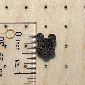 K&ouml;nnte beinhalten: Ein dunkelbrauner Holz-Knopf mit einem schwarz-wei&szlig;en Cartoon-Bild von Mickey Mouse's Gesicht. Der Knopf hat einen Durchmesser von etwa 1,25 cm.