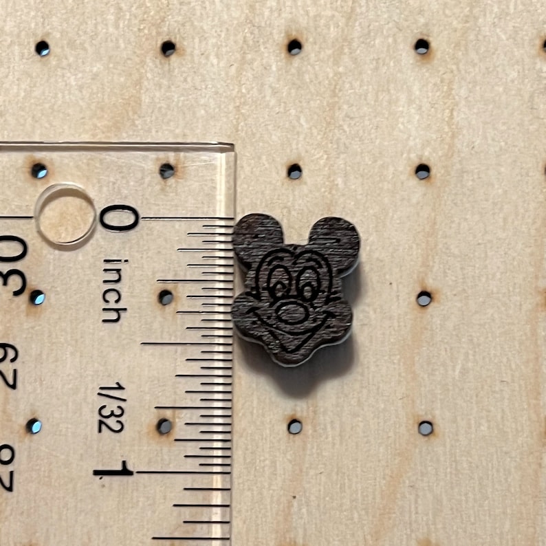 K&ouml;nnte beinhalten: Ein dunkelbrauner Holz-Knopf mit einem schwarz-wei&szlig;en Cartoon-Bild von Mickey Mouse's Gesicht. Der Knopf hat einen Durchmesser von etwa 1,25 cm.