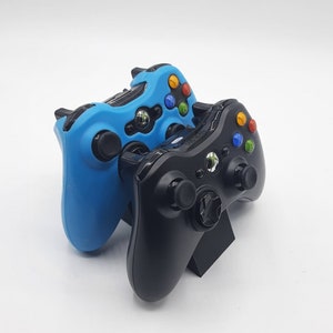 Könnte beinhalten: Zwei Videospiel-Controller, einer blau und einer schwarz, werden auf einem Ständer präsentiert. Die Controller sind beide Xbox 360-Controller.