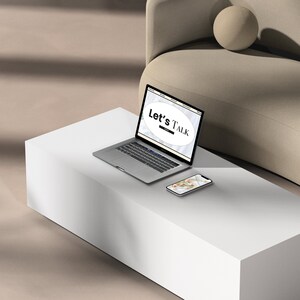 Puede incluir: Un ordenador portátil blanco con un sitio web abierto en la pantalla. El sitio web tiene un círculo blanco con el texto "Let's Talk" en negro. El ordenador portátil está sobre una mesa blanca con un teléfono inteligente blanco al lado.