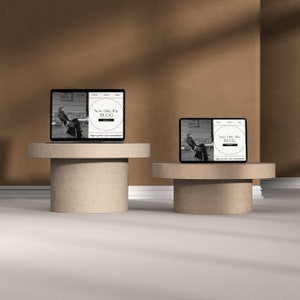 May include: Two laptops with web pages open on them are displayed on two beige cylindrical pedestals. The web pages are both titled "New One the BLOG" and feature a black and white photo of a person sitting in a chair. The laptops are on a beige surface with a brown wall in the background.