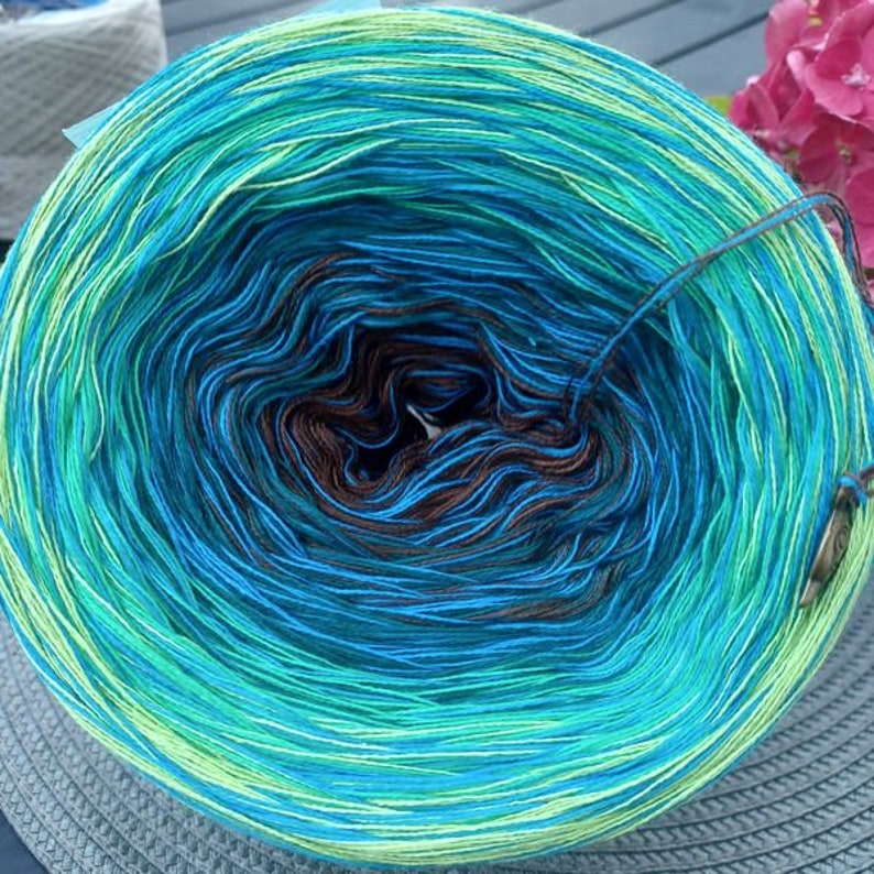 May include: A skein of yarn with a gradient of green, blue, and brown colors. The yarn is wound into a ball shape and is ready to be used for knitting or crocheting.