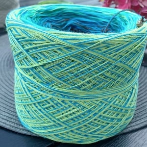 May include: A skein of yarn with a green and blue color gradient. The yarn is wound into a ball shape and is ready for knitting or crocheting.