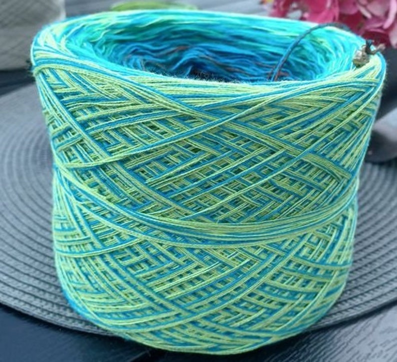 May include: A skein of yarn with a green and blue color gradient. The yarn is wound into a ball shape and is ready for knitting or crocheting.