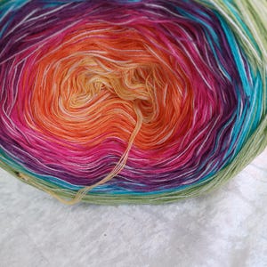 Könnte beinhalten: Nahaufnahme eines lebendigen Knäuels Garn mit Farbverlauf. Das Garn wechselt von Grün zu Türkis, Lila, Pink, Orange und Gelb. Weiße Strähnen sind im farbenfrohen Garn eingestreut.