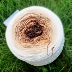 Könnte beinhalten: Eine Garnrolle mit einem weißen und braunen Farbverlauf. Das Garn ist zu einer Kugel gewickelt und bereit zum Stricken oder Häkeln.