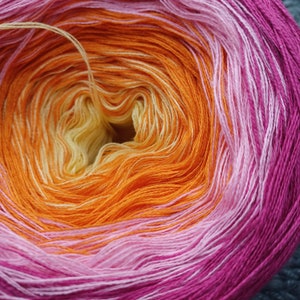 Könnte beinhalten: Nahaufnahme eines lebendigen Garnknäuels mit Farbverlauf. Das Garn wechselt von Gelb zu Orange, dann zu Rosa und schließlich zu einem tiefen Magenta. Das Garn ist eng gewickelt, mit einem Faden, der sich aus der Mitte erstreckt.