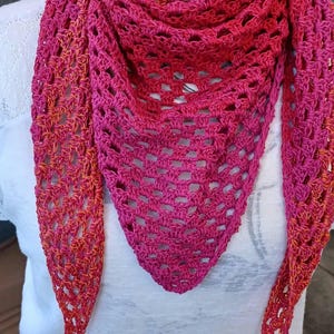 Könnte beinhalten: Ein handgehäkelter Schal in Rosa- und Orangetönen. Der dreieckige Schal hat ein offenes, durchbrochenes Muster und einen Farbverlauf, der von tiefem Rosa zu Orange übergeht. Die Enden des Schals haben eine Quaste.