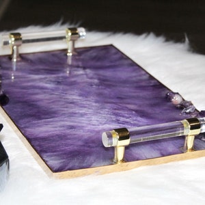May include: A rectangular serving tray with a purple resin base and gold trim. The tray has two clear acrylic handles with gold accents. The tray is decorated with small amethyst crystals.
