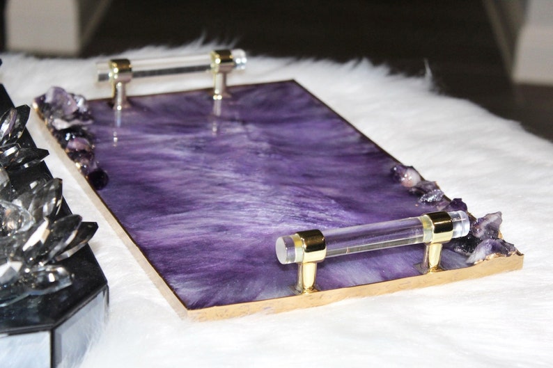 May include: A rectangular serving tray with a purple resin base and gold trim. The tray has two clear acrylic handles with gold accents. The tray is decorated with small amethyst crystals.