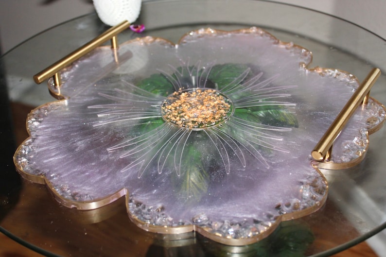 May include: A light purple resin serving tray with gold accents and a flower design. The tray has two gold handles and a clear center with gold flakes.