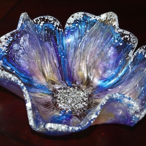 May include: A blue, purple and white resin flower bowl with a silver glitter rim. The bowl is shaped like a flower with five petals.