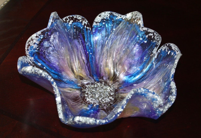 May include: A blue, purple and white resin flower bowl with a silver glitter rim. The bowl is shaped like a flower with five petals.