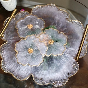 May include: A white resin serving tray with a floral design and gold accents. The tray has two gold handles and is perfect for serving snacks or drinks.