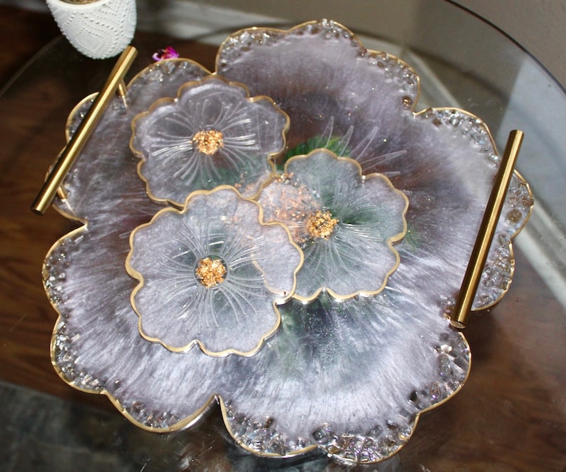 May include: A white resin serving tray with a floral design and gold accents. The tray has two gold handles and is perfect for serving snacks or drinks.
