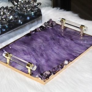 May include: A rectangular serving tray with a purple resin base and gold trim. The tray has two clear acrylic handles and is decorated with amethyst crystals.