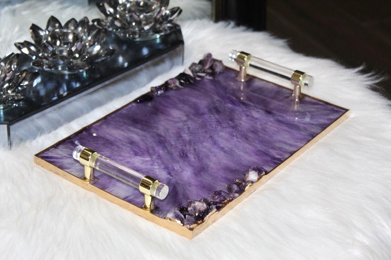 May include: A rectangular serving tray with a purple resin base and gold trim. The tray has two clear acrylic handles and is decorated with amethyst crystals.