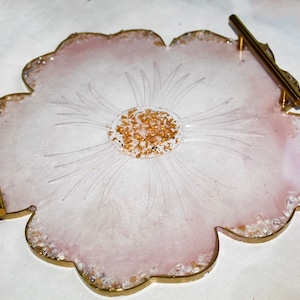 May include: A pink resin serving tray with a flower design and gold glitter accents. The tray has two gold metal handles.