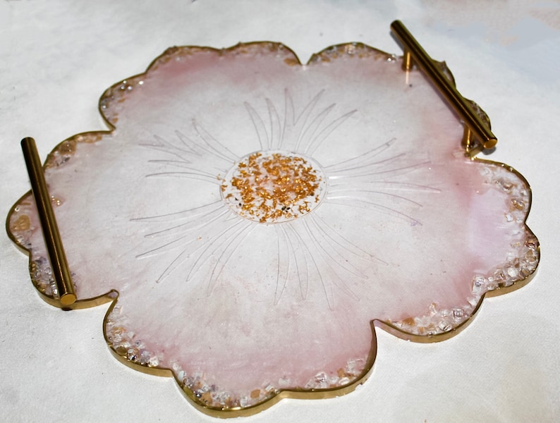 May include: A pink resin serving tray with a flower design and gold glitter accents. The tray has two gold metal handles.