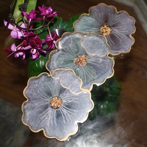 May include: Three gray resin coasters with a gold rim and a floral design. Each coaster features a raised flower with a gold glitter center.